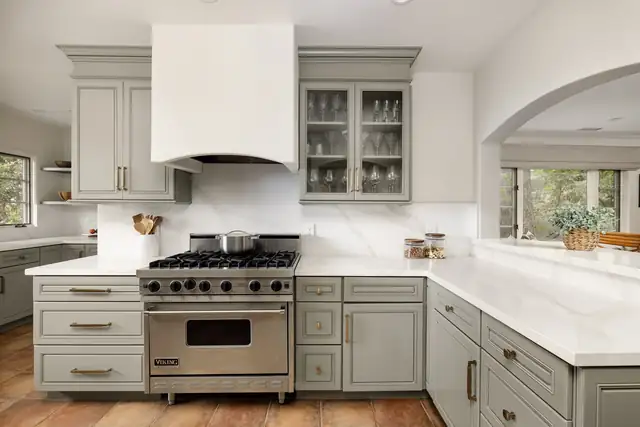 Kitchen with sage green cabinets, a white plaster hood, a professional range and an arched opening to the dining room