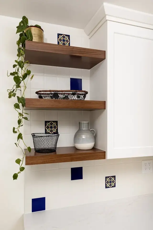 Walnut floating shelves beside white cabinetry with blue accent tile in a Santa Barbara kitchen remodel