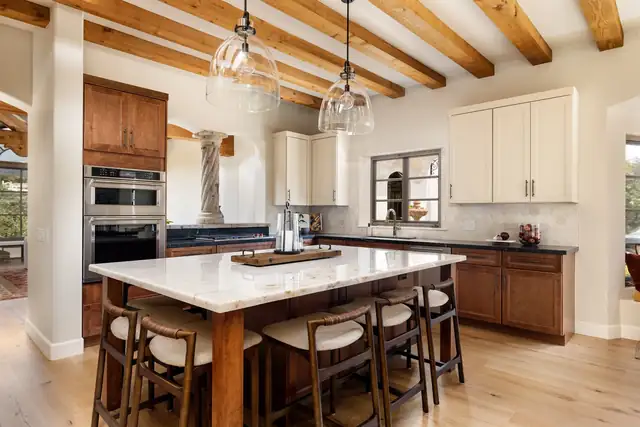 Italian Villa style Santa Barbara kitchen with quartzite island, wood beams, double wall ovens and cream upper cabinets
